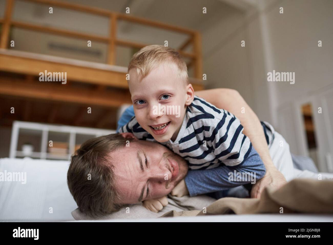 Portrait d'un garçon joyeux et excité avec des cheveux blonds qui se battent avec le père tout en s'amusant à la maison Banque D'Images