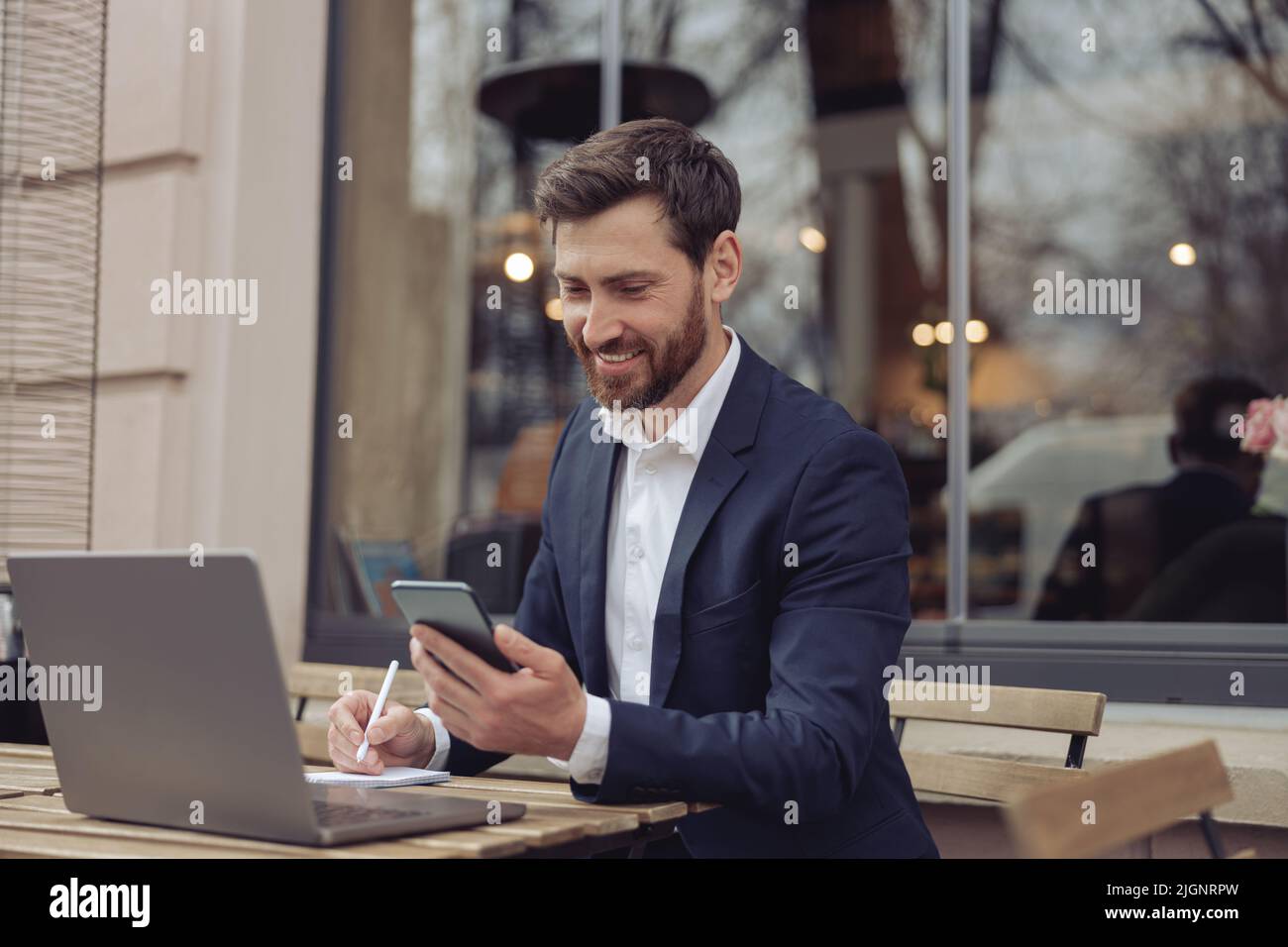 Homme d'affaires joyeux dans un style élégant assis dans un café. Travail de planification avec téléphone, ordinateur portable et notes. Banque D'Images