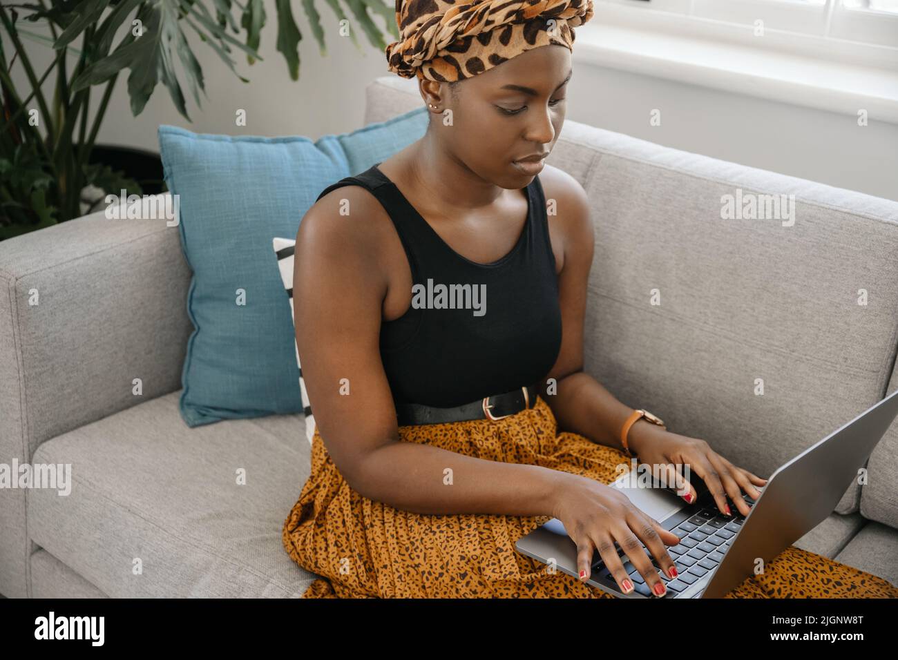 Gros plan belle femme africaine traditionnelle jeune génération z assise sur un canapé à la maison, dactylographiant sur un ordinateur portable, souriant, tourné avec un espace de copie Banque D'Images