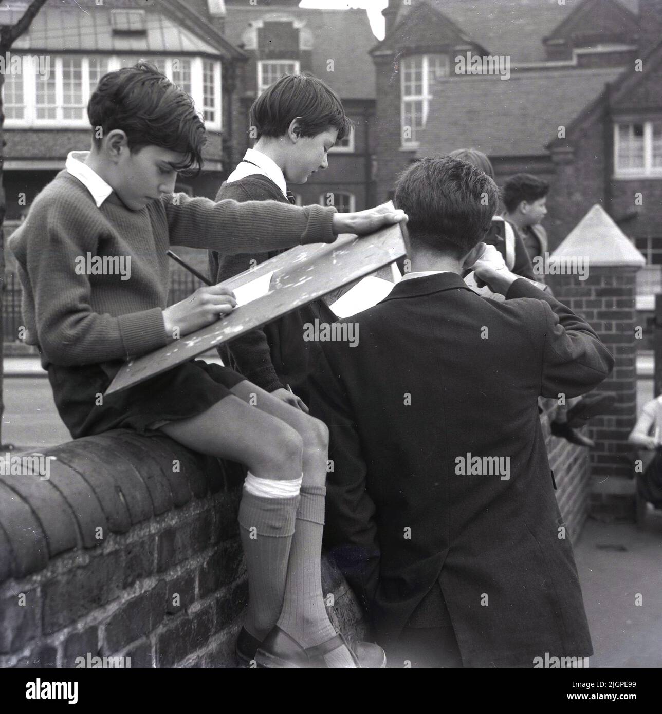 1960s, historique, cours d'art, hors école dans la banlieue de Londres, un écolier en short assis sur un mur, dessin. Banque D'Images