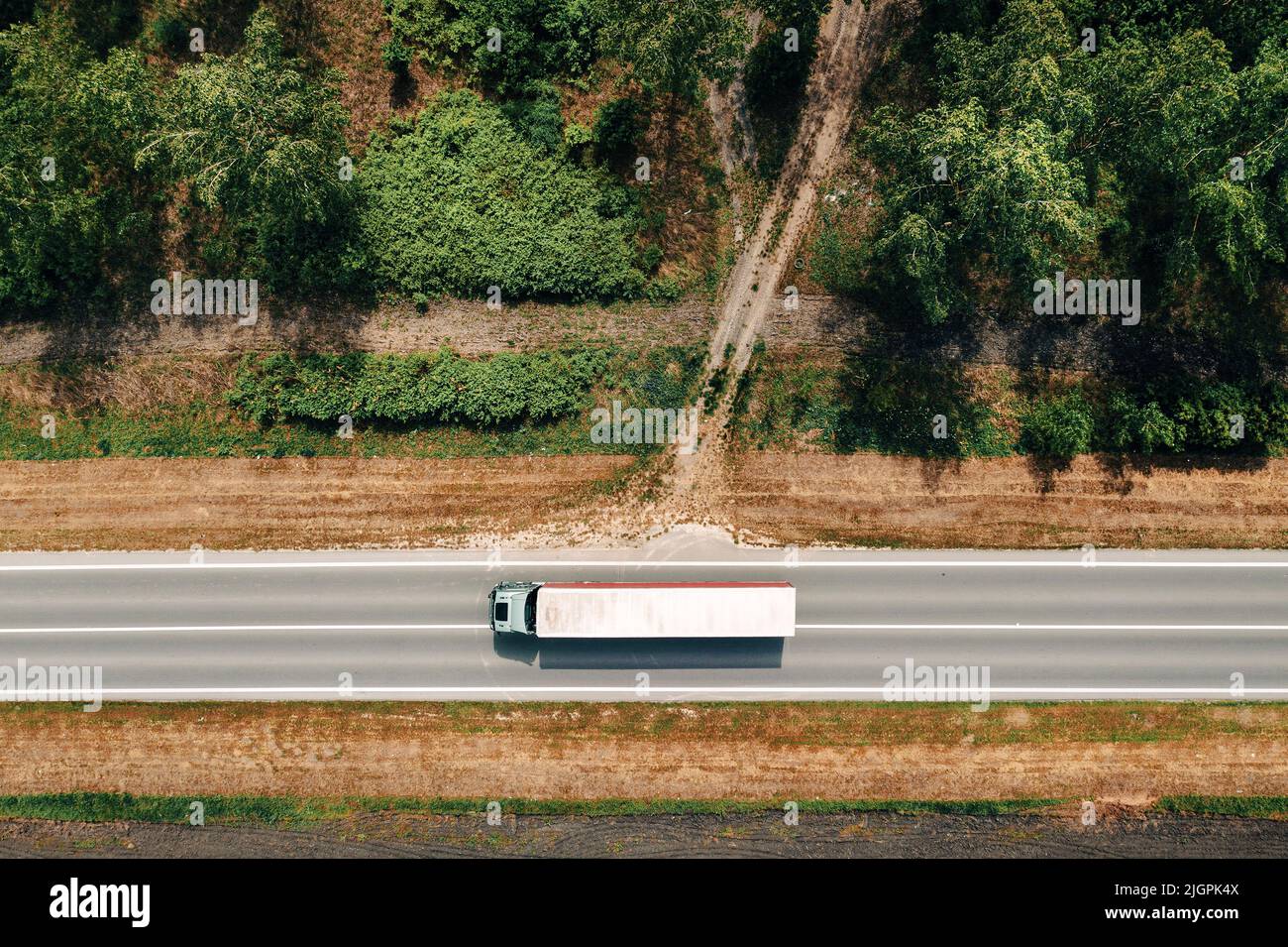 Photo aérienne de semi-camion conduisant le long de l'autoroute à travers le paysage de campagne, drone pov directement au-dessus le jour ensoleillé de printemps. Transport et lo Banque D'Images