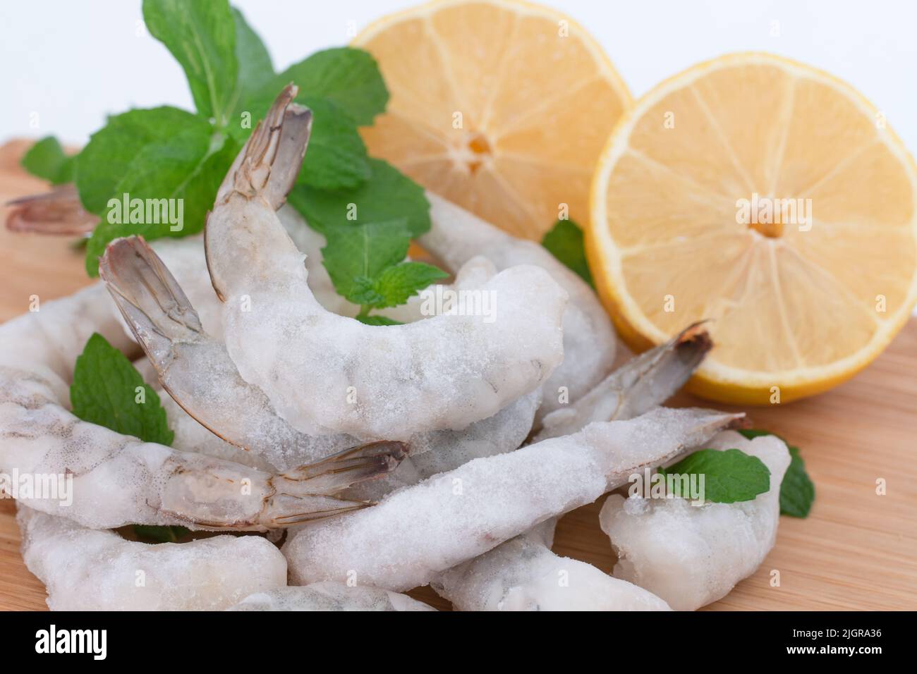 Crevettes crues congelées pelées sur une planche à découper en bois avec des herbes et du citron. Banque D'Images