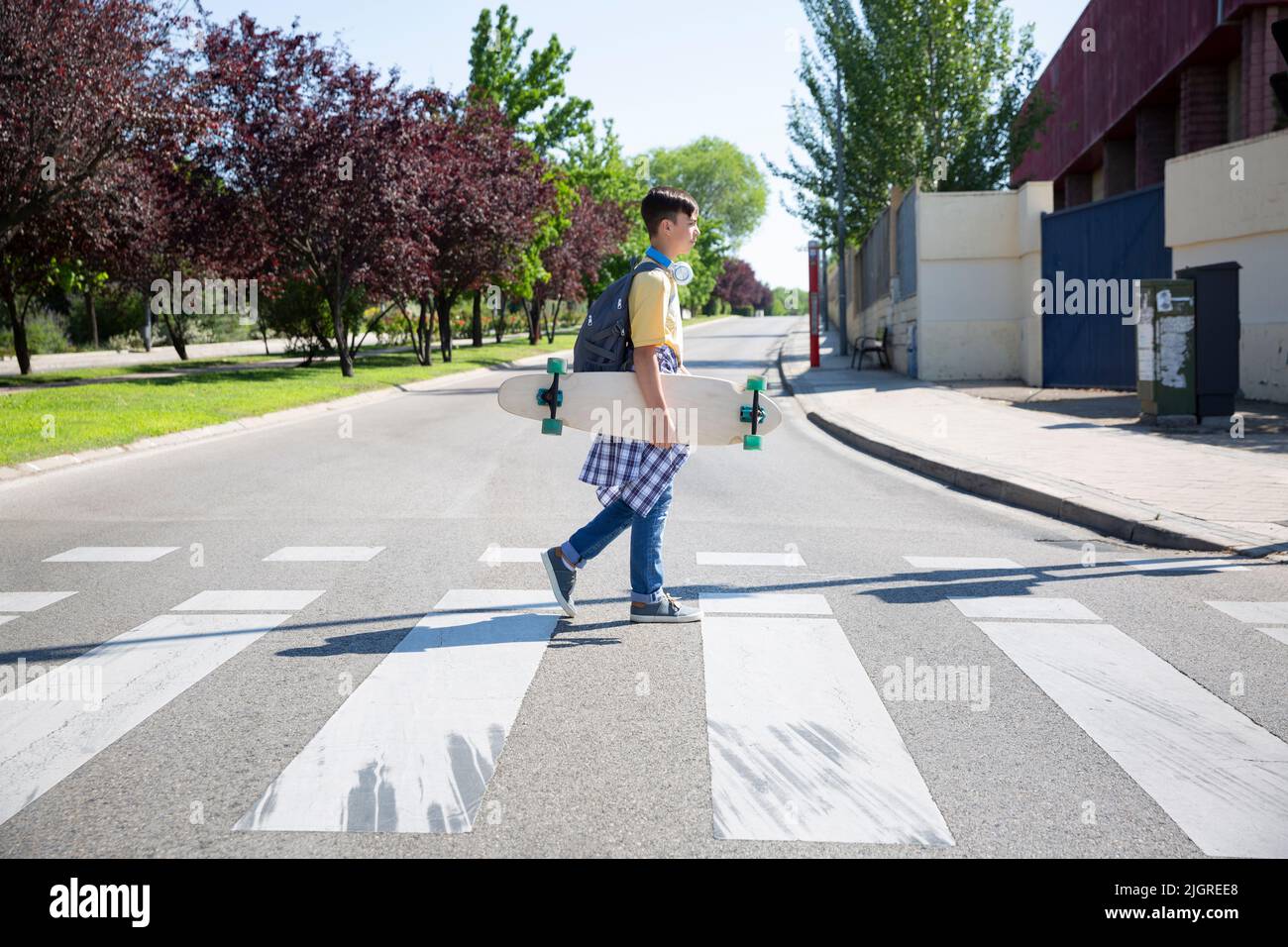 Garçon étudiant de lycée avec longue planche à roulettes croisant la rue. Espace pour le texte. Banque D'Images