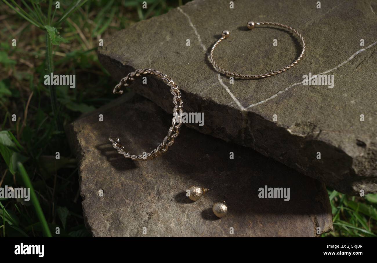 Vue de dessus de bracelets dorés brillants et boucles d'oreilles paire sur pierre naturelle Banque D'Images