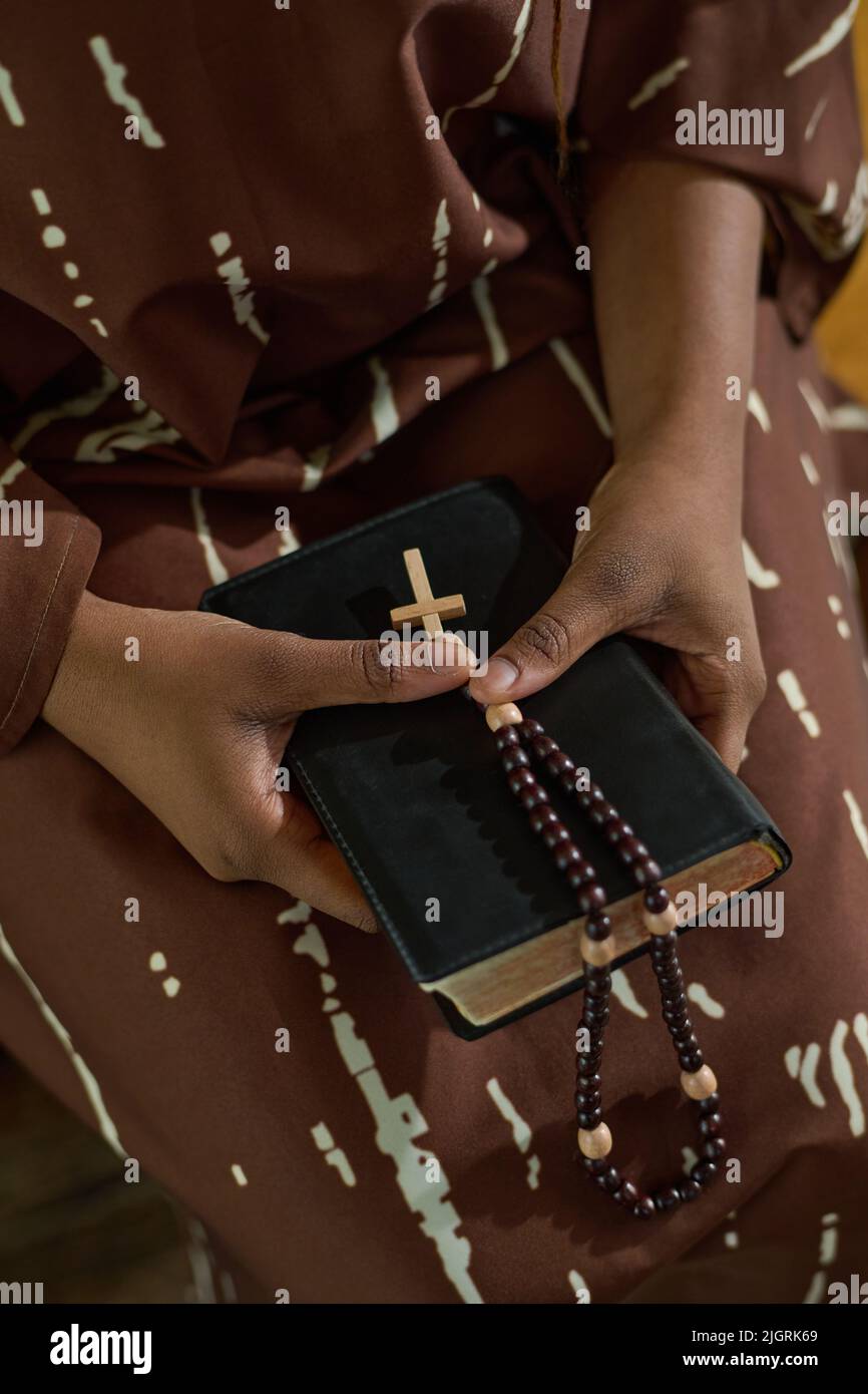 Mains de jeune femme noire en robe brune tenant la Bible et les perles rosaires avec une petite croix en bois tout en assistant au service de l'église Banque D'Images