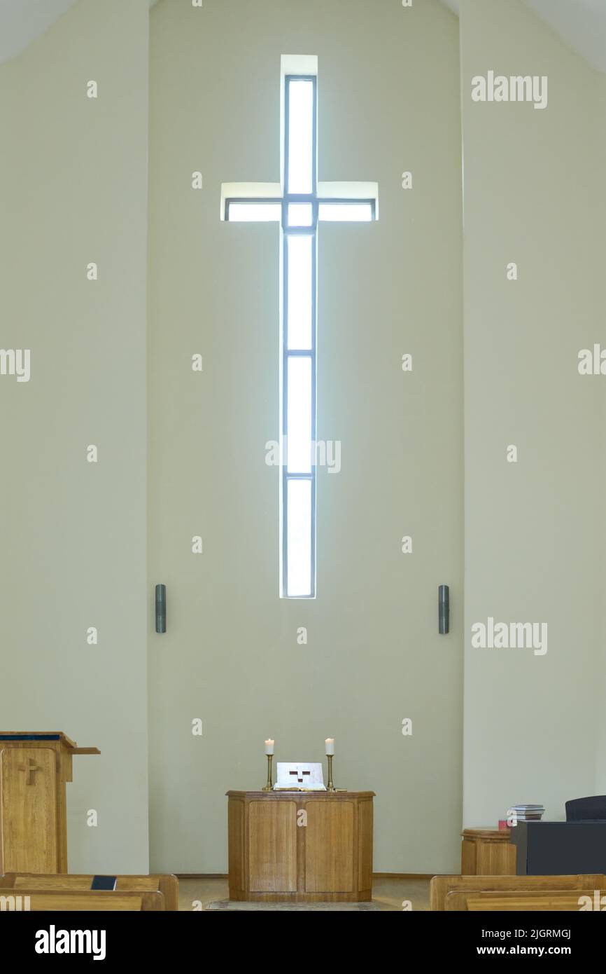 Salle de service vide dans l'église catholique ou évangélique moderne avec croix sur le mur au-dessus de la chaire en bois avec autel et deux bougies Banque D'Images