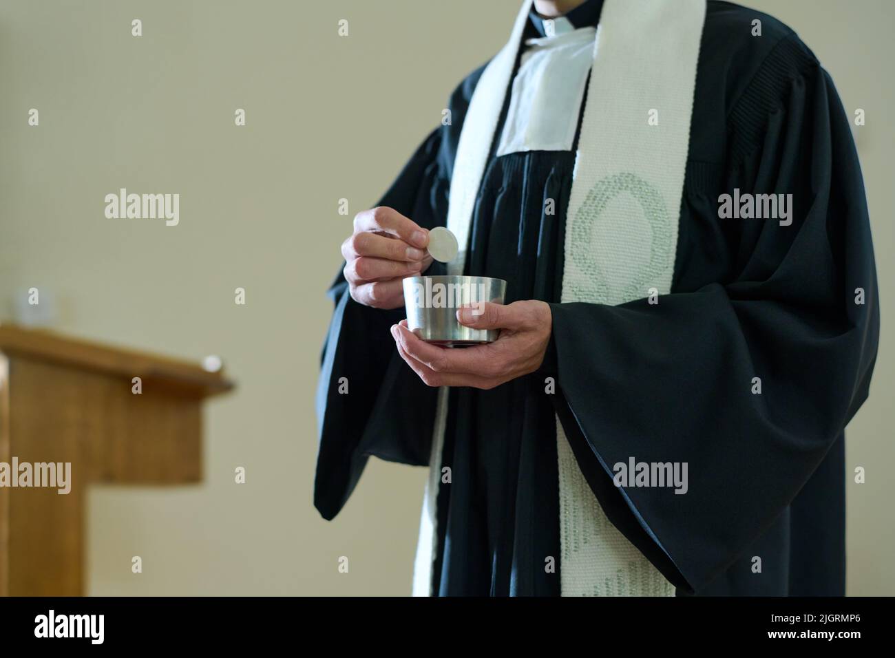 Prêtre de l'église catholique en cassock tenant une petite tasse avec du pain sans levain pour le rite de communion des paroissiens pendant la liturgie Banque D'Images