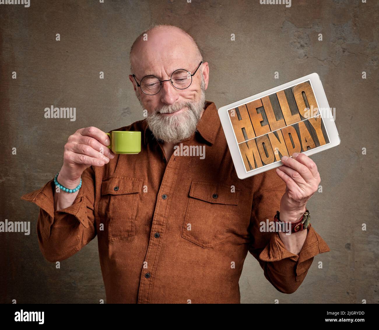 Bonjour lundi - un homme senior souriant boit du café et montre une tablette numérique avec du texte en bois, début positif d'un nouveau concept de semaine de travail Banque D'Images