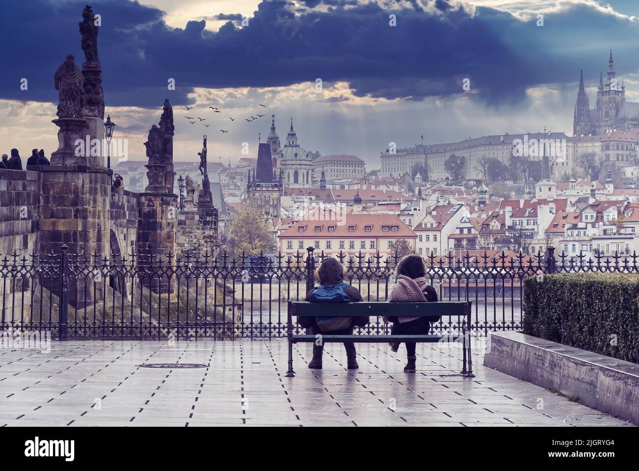 Quelques jeunes assis sur le banc, regardant le Hradcany de Prague avec une vue partielle sur le pont Charles et la Vltava Banque D'Images