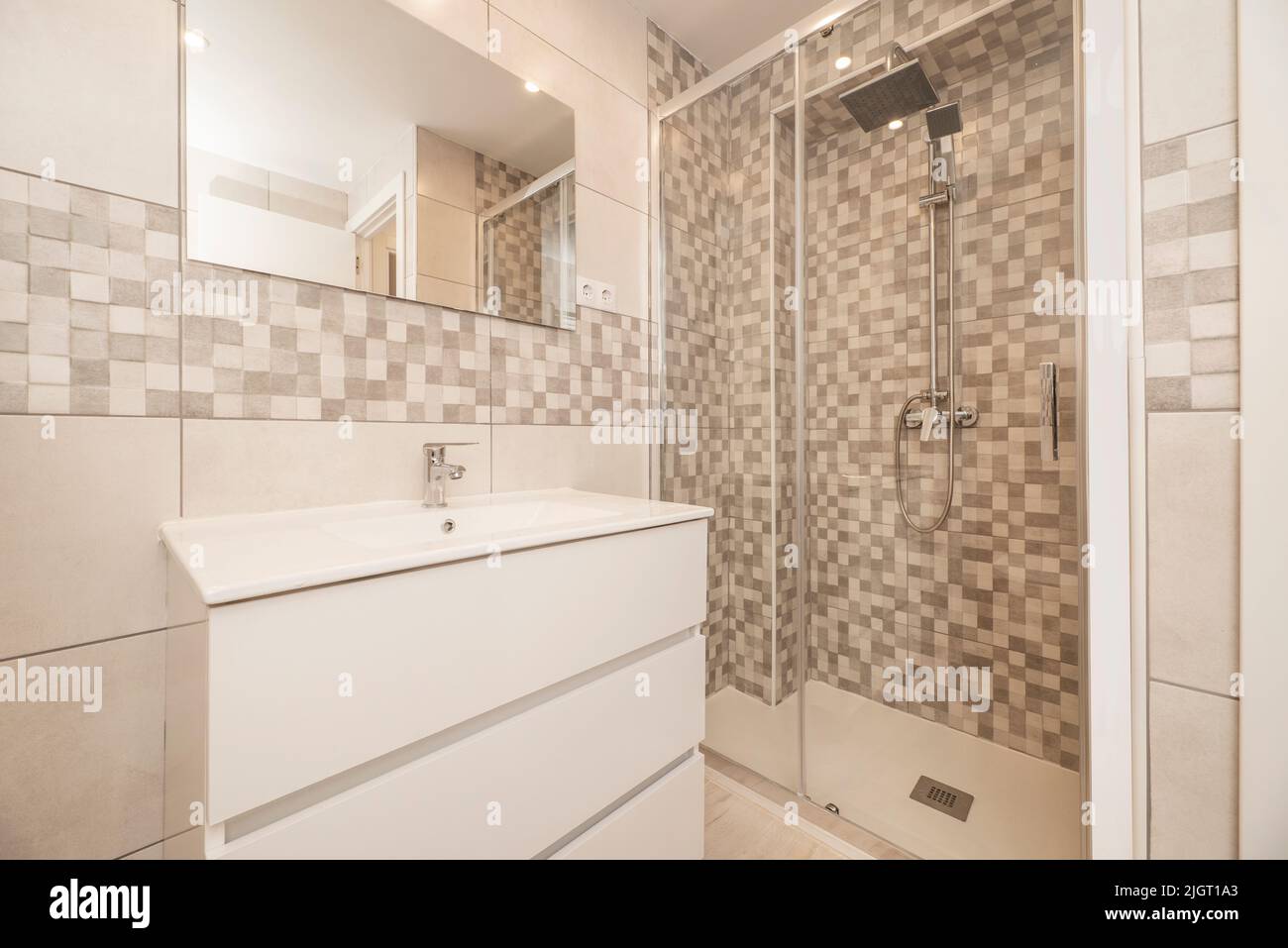 Petite salle de bains moderne avec miroir sans cadre au mur, cabine de douche avec porte coulissante en verre et commode blanche Banque D'Images