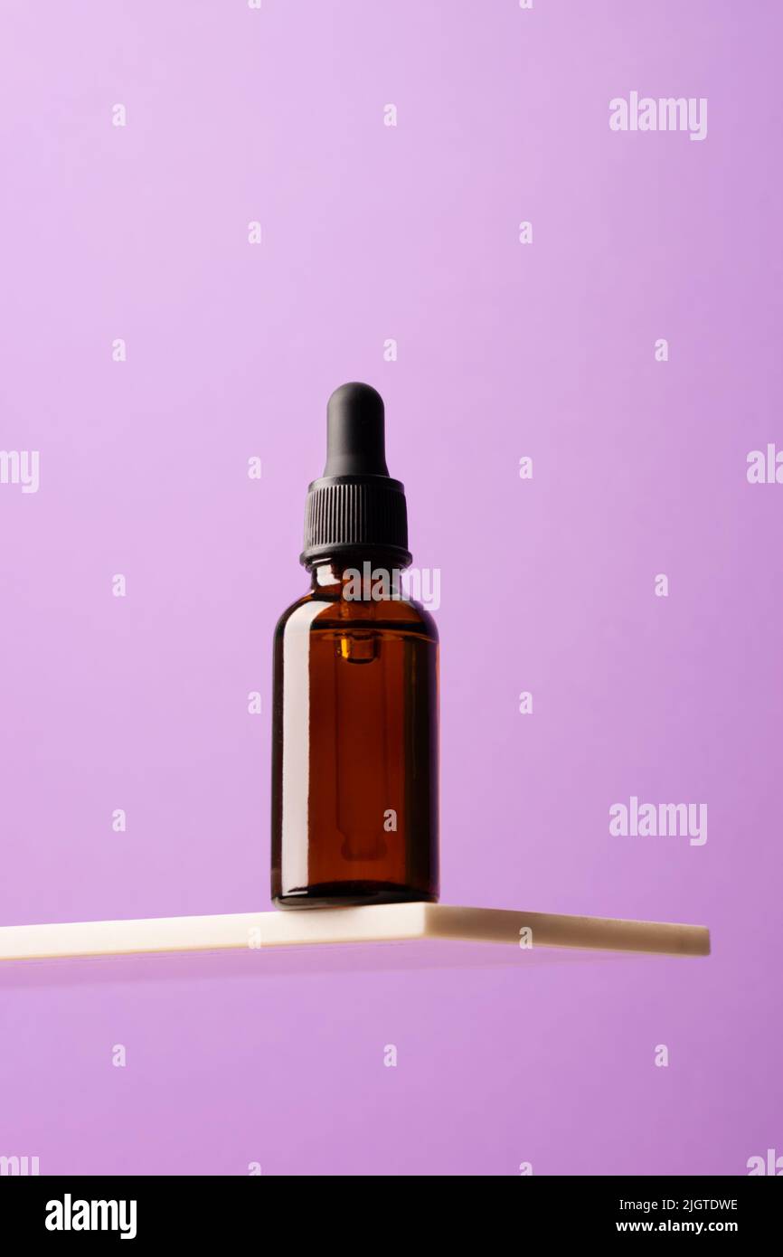 Bouteille de produit cosmétique, verre foncé avec étagère en marbre créatif pour pipettes, fond violet podium Banque D'Images