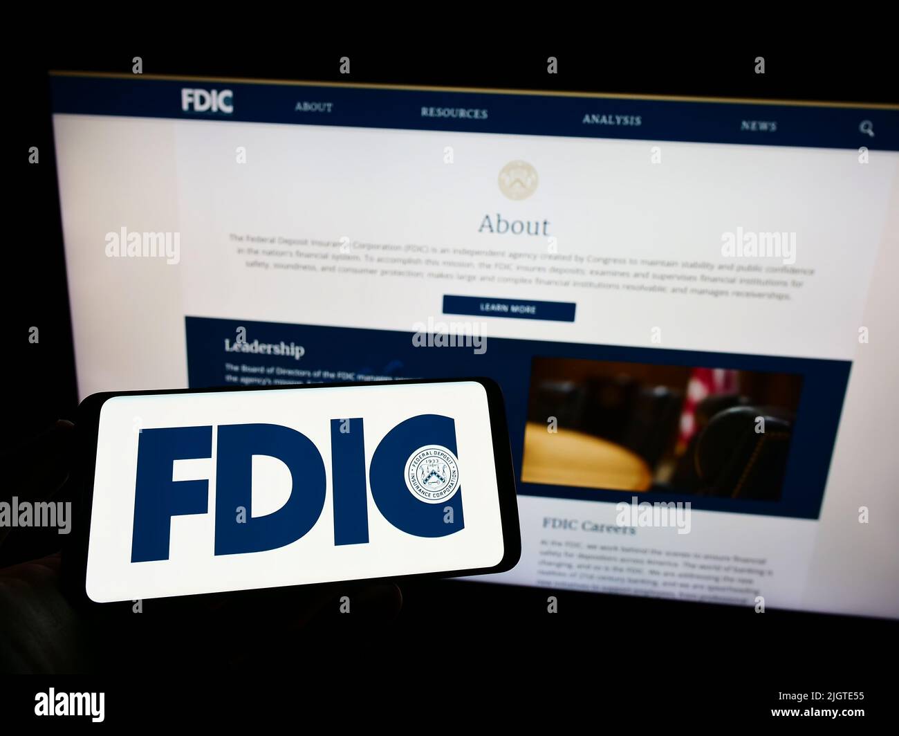 Personne tenant un téléphone portable avec le logo de la US Federal Deposit Insurance Corporation (FDIC) à l'écran en face de la page Web. Mise au point sur l'affichage du téléphone. Banque D'Images