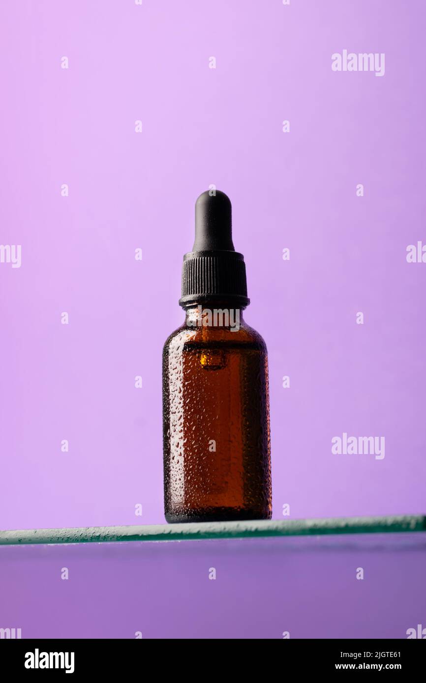 Bouteille de produit cosmétique, verre foncé avec pipette sur étagère en verre, fond violet, regarder vers le haut Banque D'Images