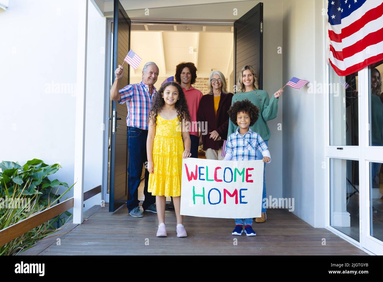 Famille multiraciale multigénération avec texte de bienvenue et drapeaux d'amérique debout à l'entrée Banque D'Images