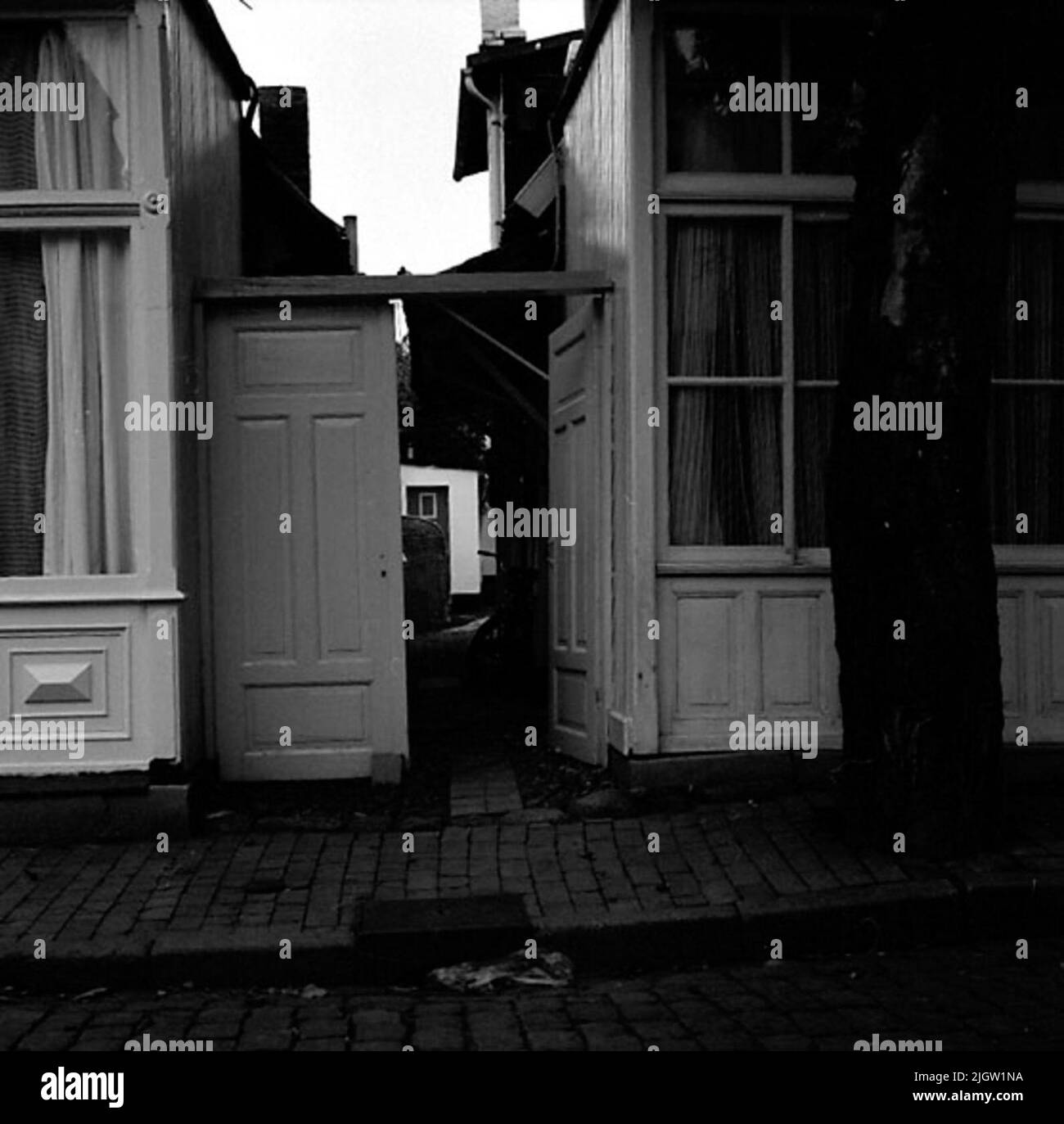 Maisons résidentielles le long d'une rue pavée. Entre les maisons se trouve une porte menant dans une allée, vers les arrière-cours. Photo de l'Allemagne (?). Banque D'Images