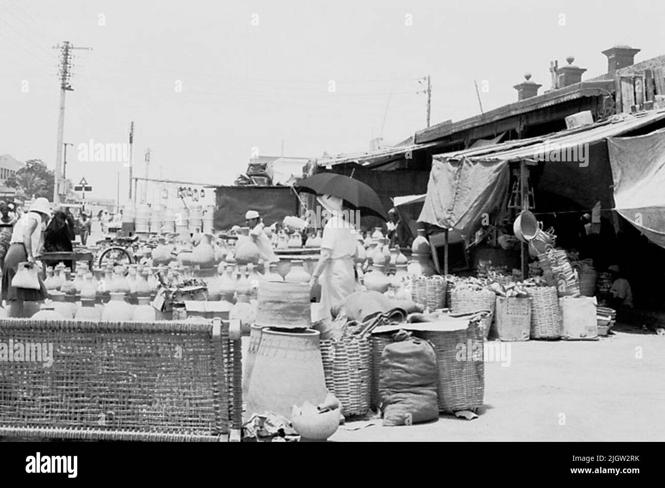 La photo a été prise vers le 1961-08-31. Il y a quelques magasins le long d'une rue d'affaires dans une communauté. L'épouse du photographe se tient et regarde la céramique à l'extérieur de l'un des magasins. Voyage africain, Aden Linjedop.36 photos en série. Banque D'Images