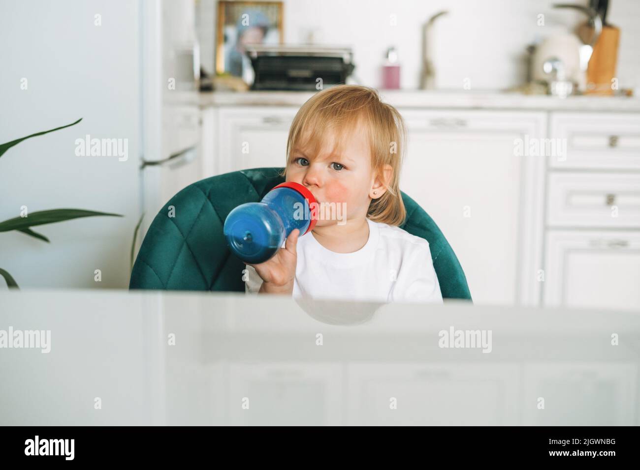 Mignonne bébé fille dans les vêtements à la maison eau potable de bouteille dans la cuisine à la maison Banque D'Images