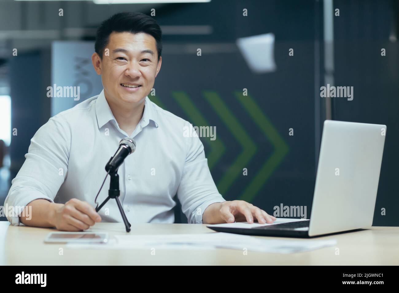 Podcast radio en ligne, entraîneur d'affaires asiatique masculin enregistrant en ligne, homme d'affaires utilisant un microphone professionnel et un ordinateur portable, portrait d'un professeur d'affaires au bureau. Banque D'Images