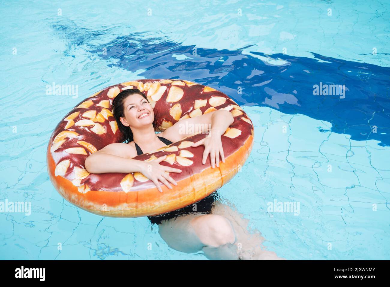 Bonne jeune femme plus la taille du corps positif en cercle donut gonflable natation dans la piscine, vacances d'été Banque D'Images