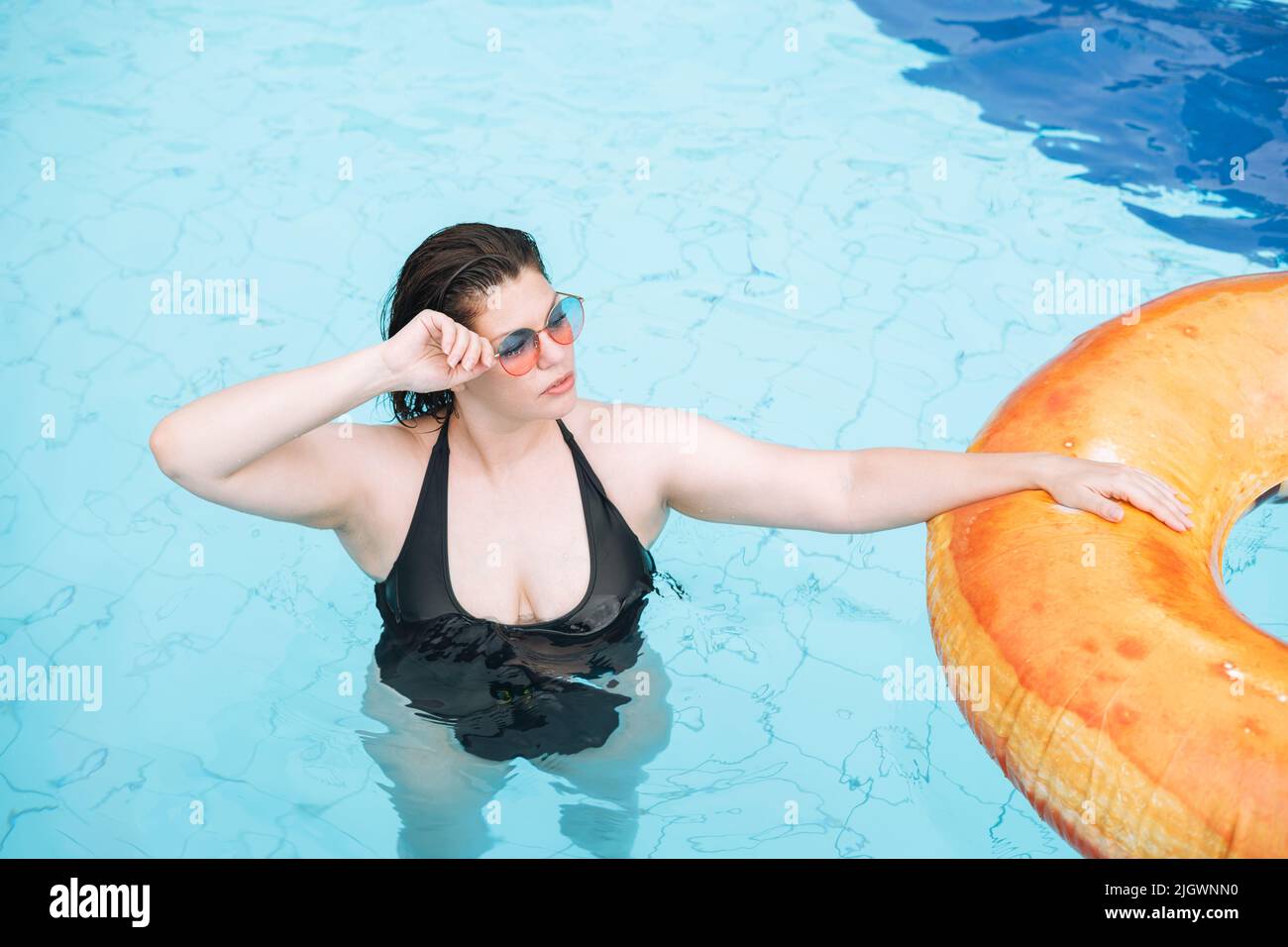 Bonne jeune femme plus la taille du corps positif en cercle donut gonflable natation dans la piscine, vacances d'été Banque D'Images