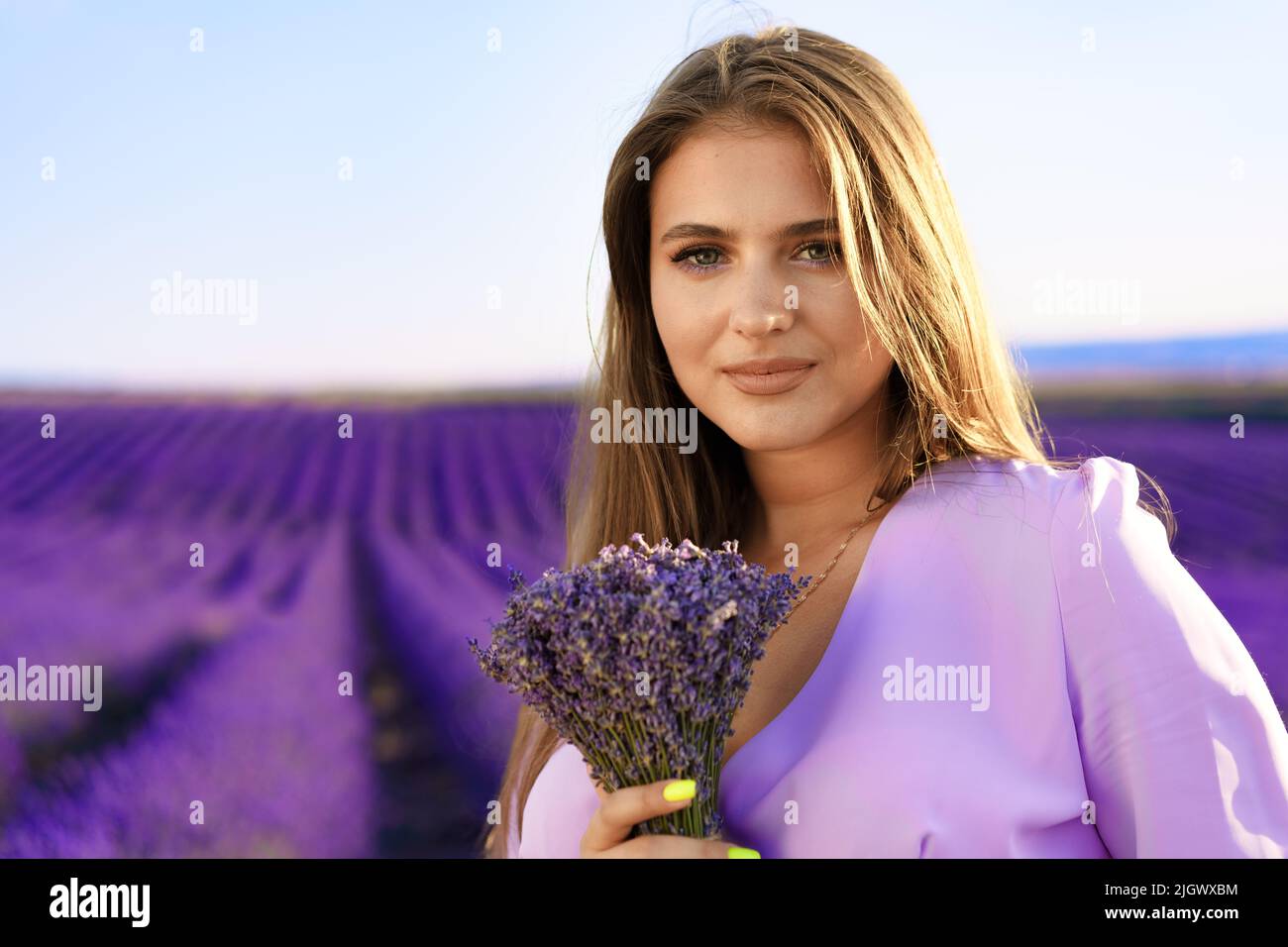 Jeune femme en robe tenant un bouquet de fleurs debout dans le champ de lavande Banque D'Images