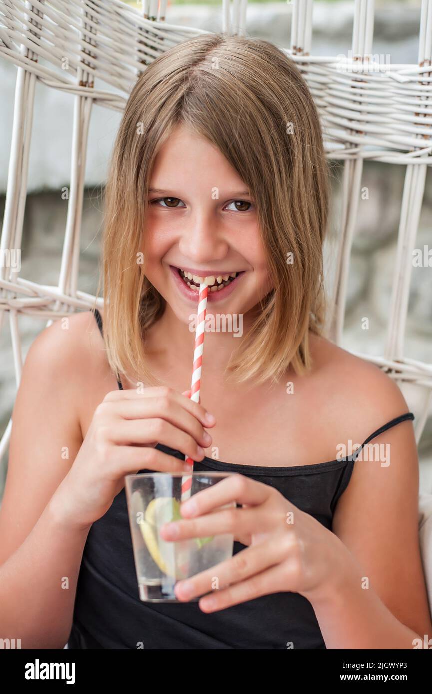 Portrait belle blonde adolescente fille boit avec de la paille du verre dans la nature. Temps libre à l'extérieur Banque D'Images