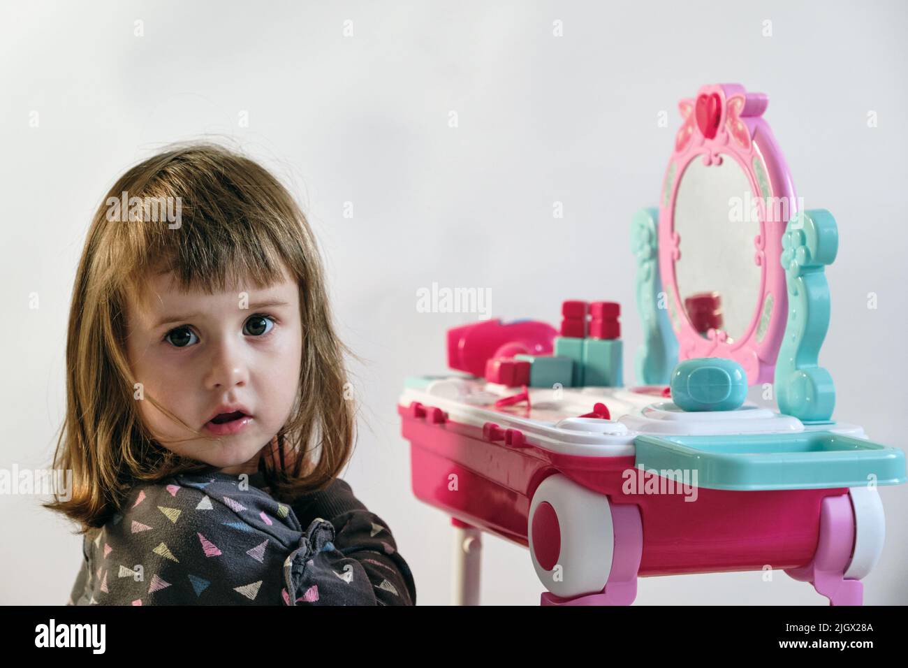 Jolie petite fille jouant avec des cosmétiques près de la table à garniture dans la chambre. 2 ans. Banque D'Images