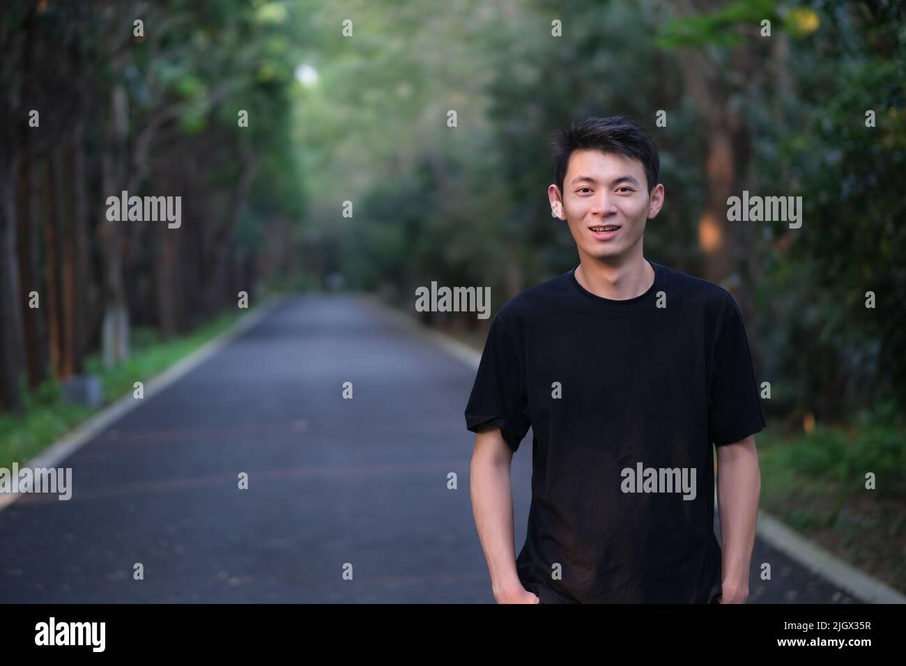 Beau jeune homme asiatique souriant et regardant l'appareil photo dans le parc naturel de la forêt Banque D'Images