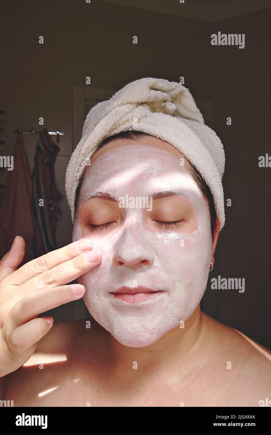 La femme Candid applique un masque d'argile, de minéraux et de sels à son visage dans la salle de bains à la maison. Soin de la peau pendant Covid-19, vraie femme, le moment de style de vie candid Banque D'Images