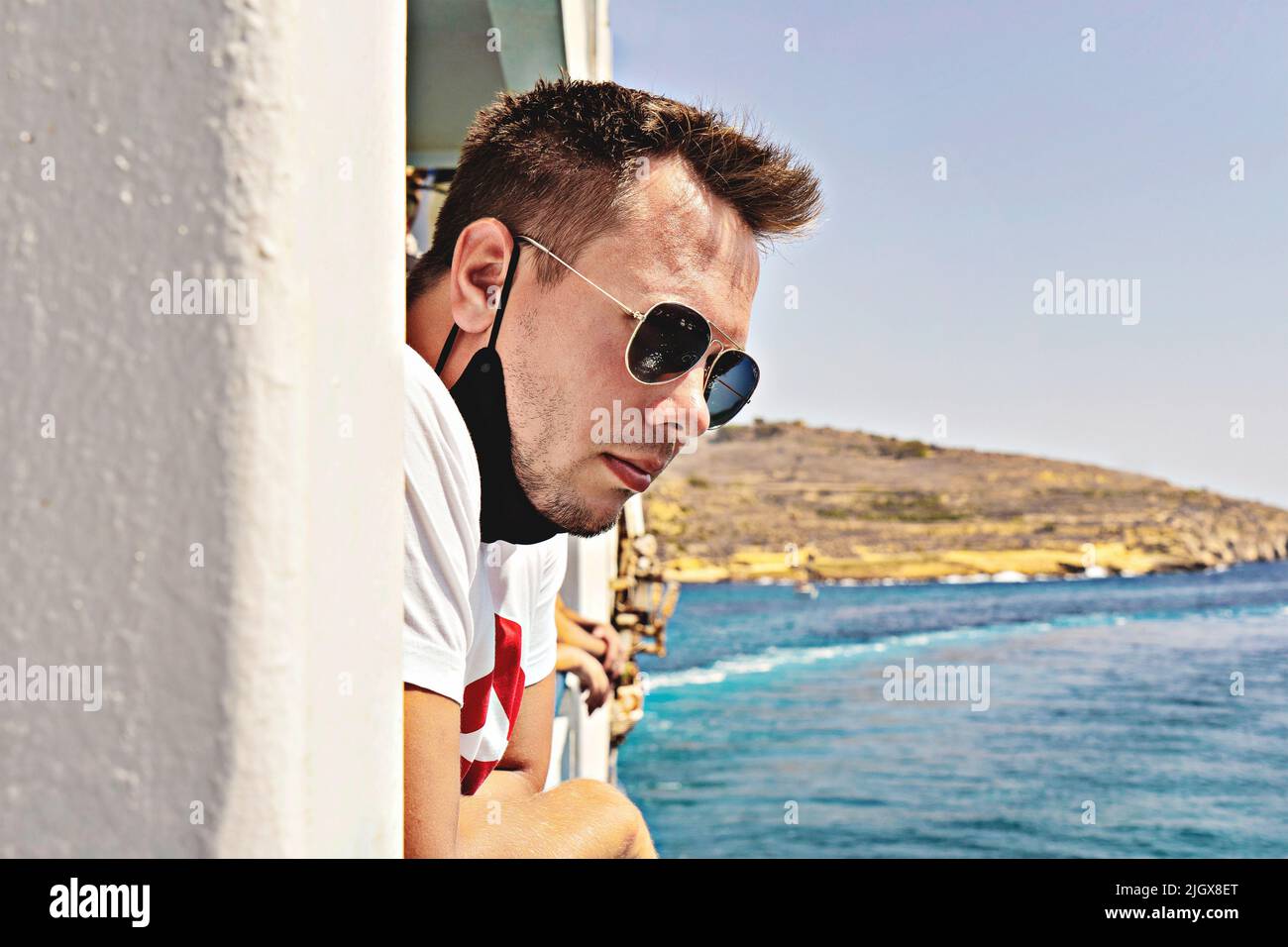 Un type attrayant en lunettes de soleil et visage sans masque profite de la brise de mer fraîche sur un ferry en mer Méditerranée pendant les voyages d'été Banque D'Images