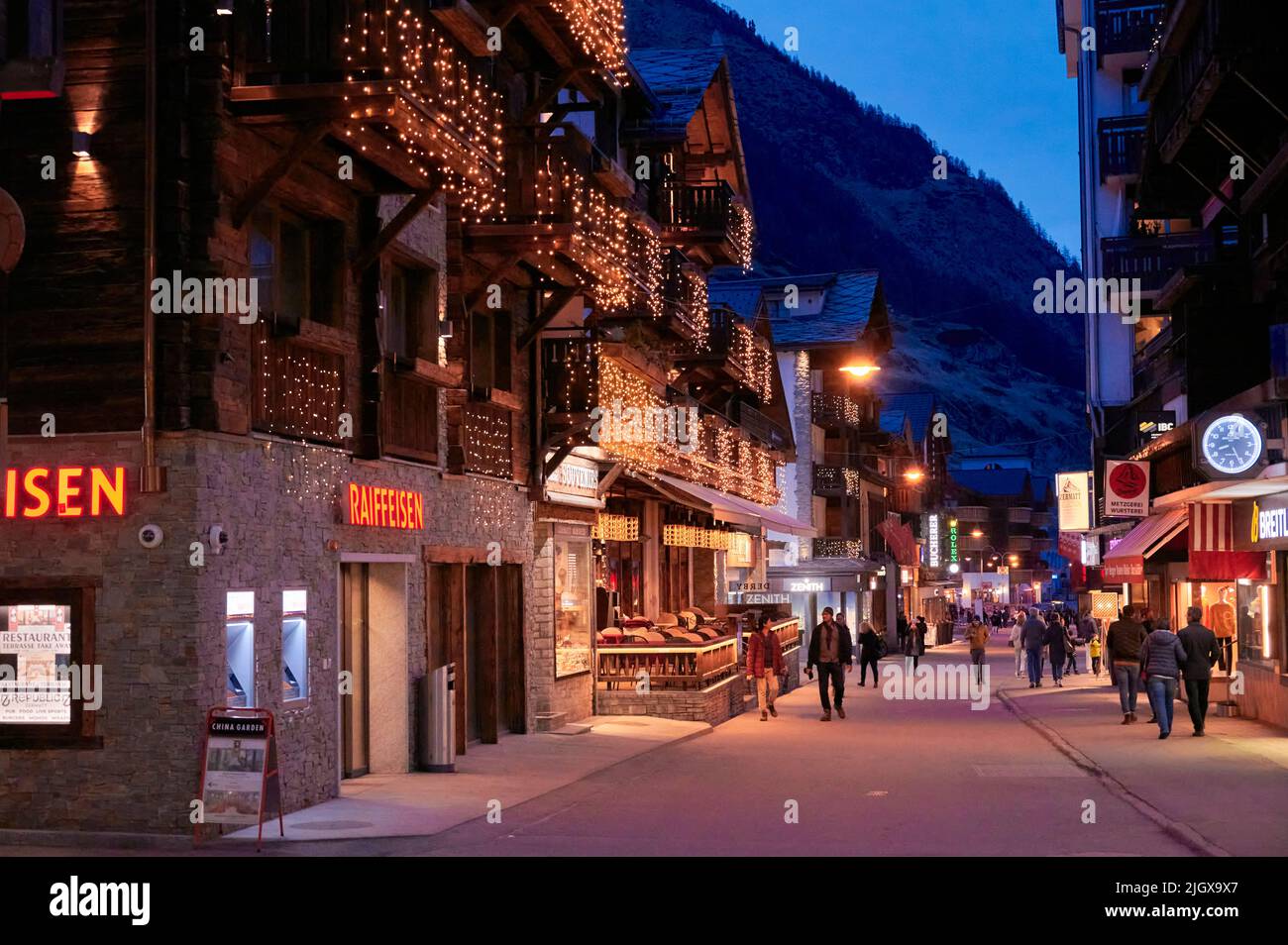 ZERMATT, SUISSE - AVR 11, 2022: Touristes marchant et visitant dans une rue de la ville de Zermatt au coucher du soleil. Banque D'Images