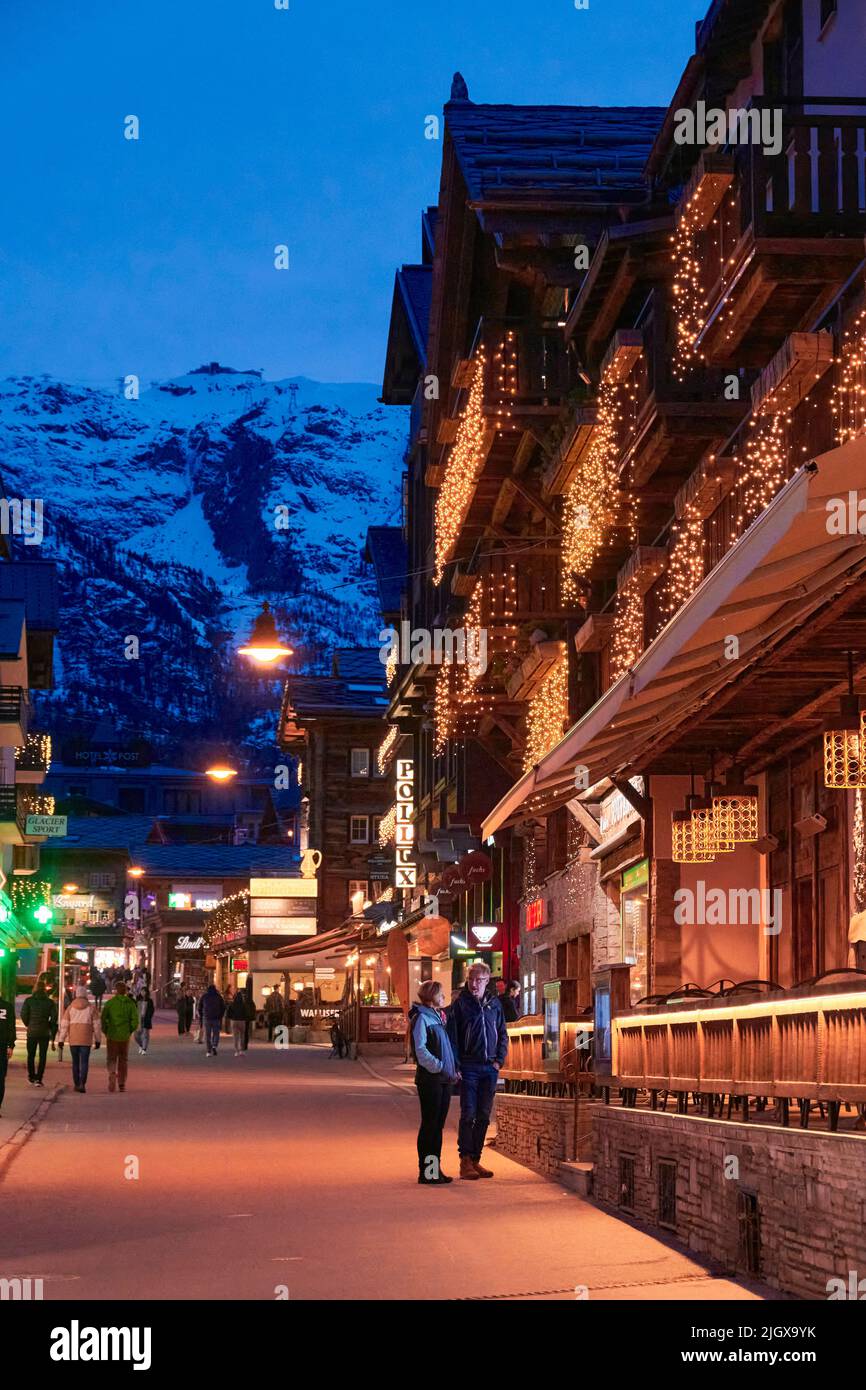 ZERMATT, SUISSE - AVR 11, 2022: Touristes marchant et visitant dans une rue de la ville de Zermatt au coucher du soleil. Banque D'Images