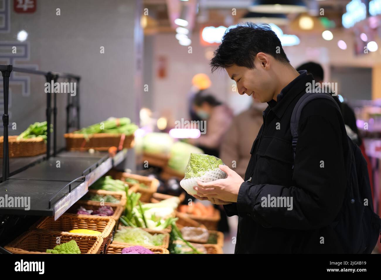 Un jeune homme asiatique cueillant des légumes dans une épicerie. Un homme souriant fait du shopping dans un supermarché Banque D'Images