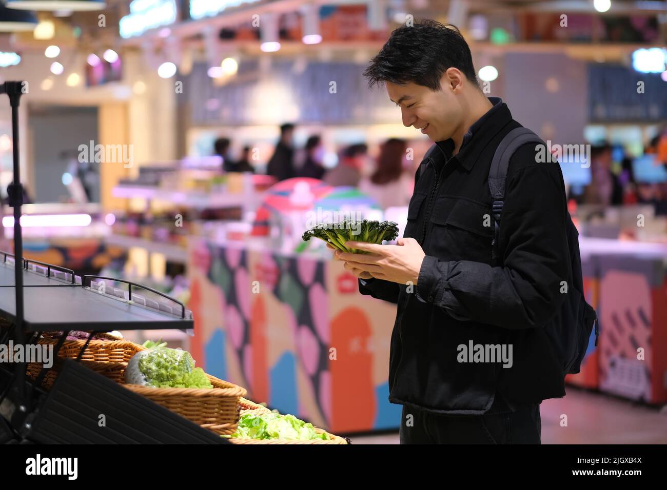 Un jeune homme asiatique souriant choisit des légumes à l'épicerie. Banque D'Images