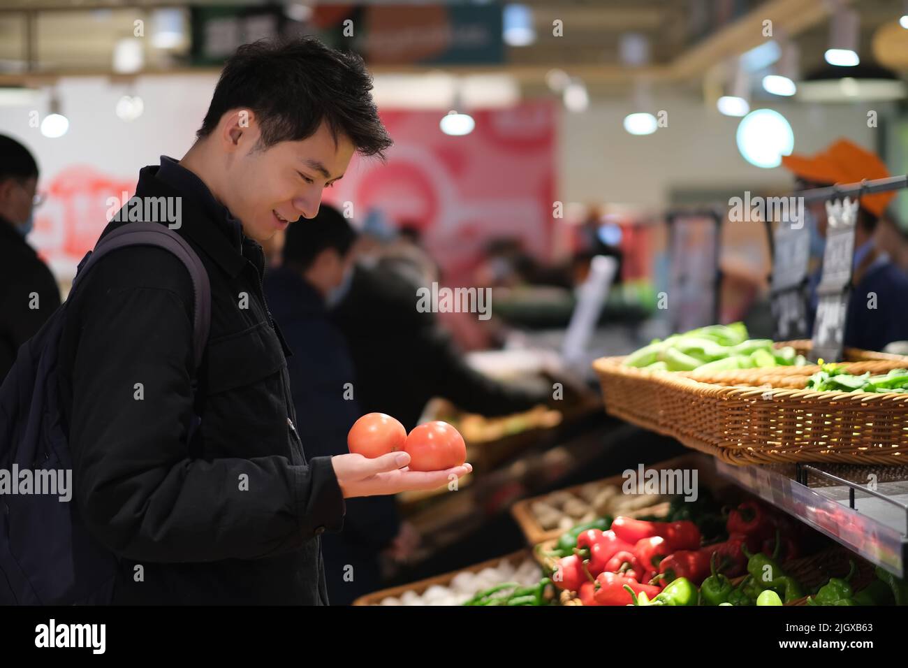 Jeune homme chinois qui vérifie les légumes de tomate à l'épicerie. Souriant, les Asiatiques magasinent dans un supermarché Banque D'Images