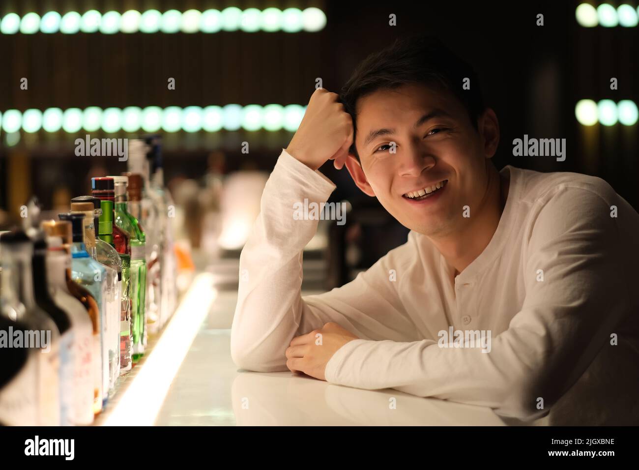 Portrait d'un jeune homme asiatique souriant assis au comptoir du bar, regardant l'appareil photo la nuit Banque D'Images