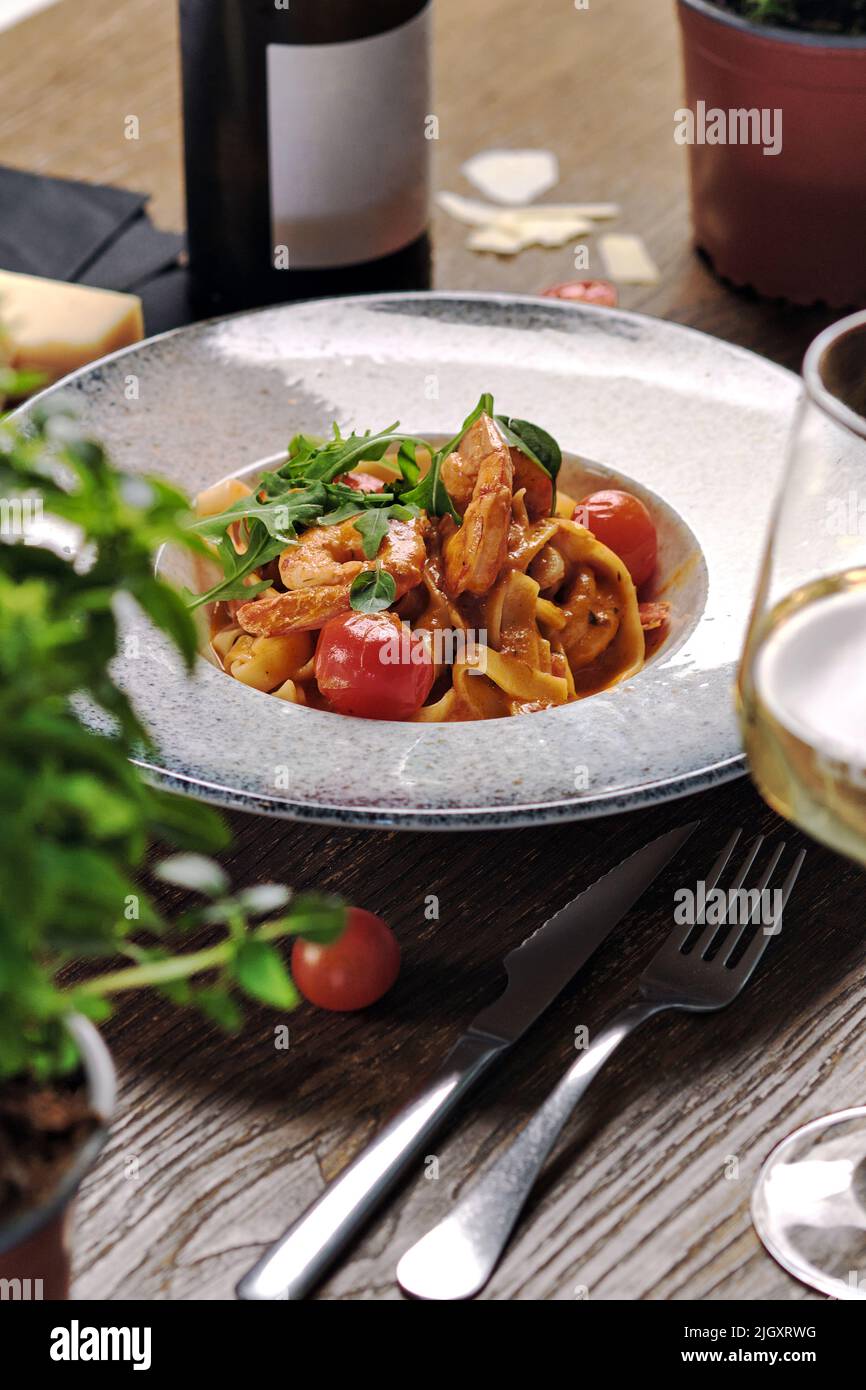 Gros plan sur des pâtes de fruits de mer avec sauce et tomates cerises servies avec du vin blanc. Plat principal, concept de plat de restaurant Banque D'Images