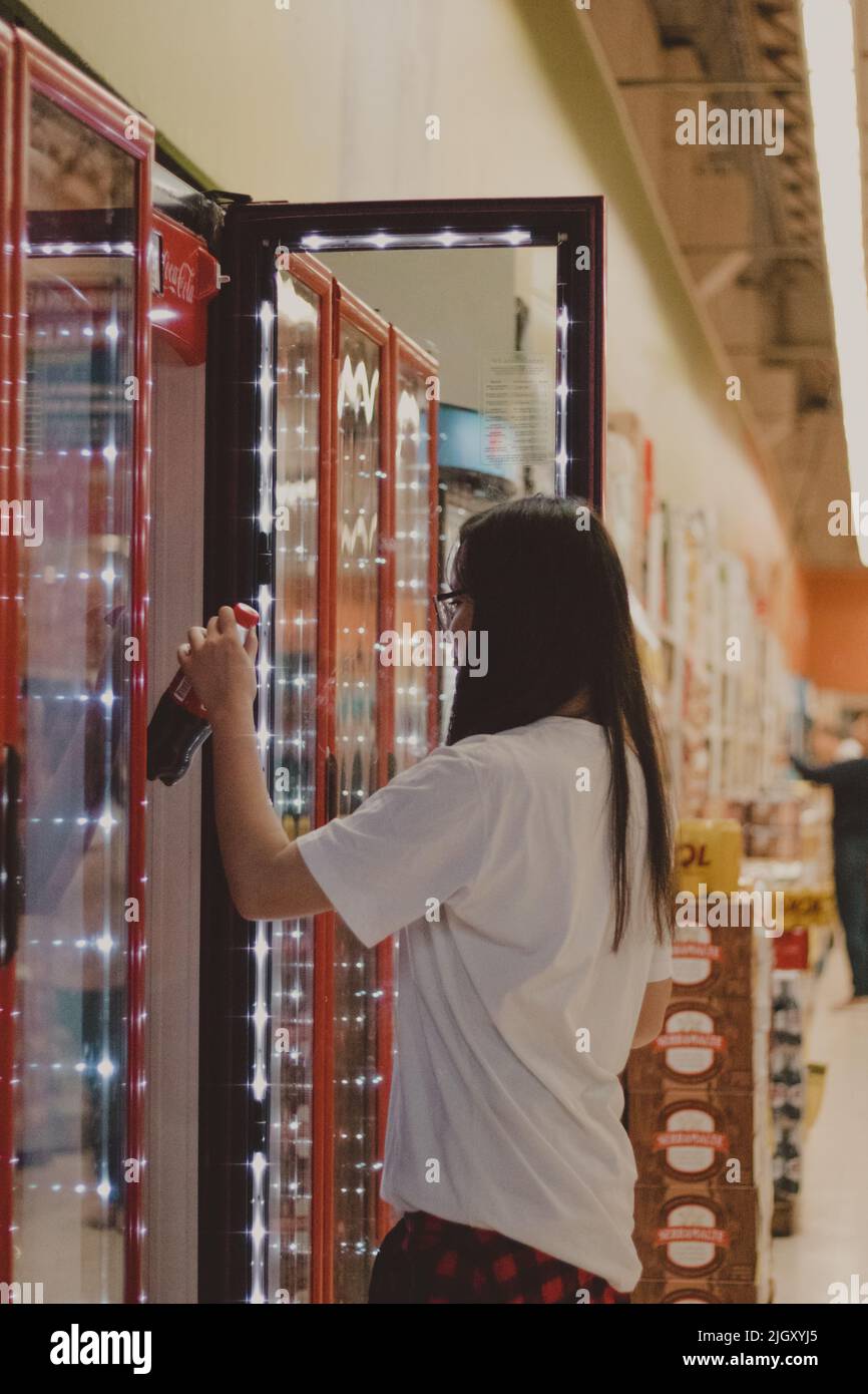 une jeune fille attrapant une bouteille de soda sur le réfrigérateur Banque D'Images