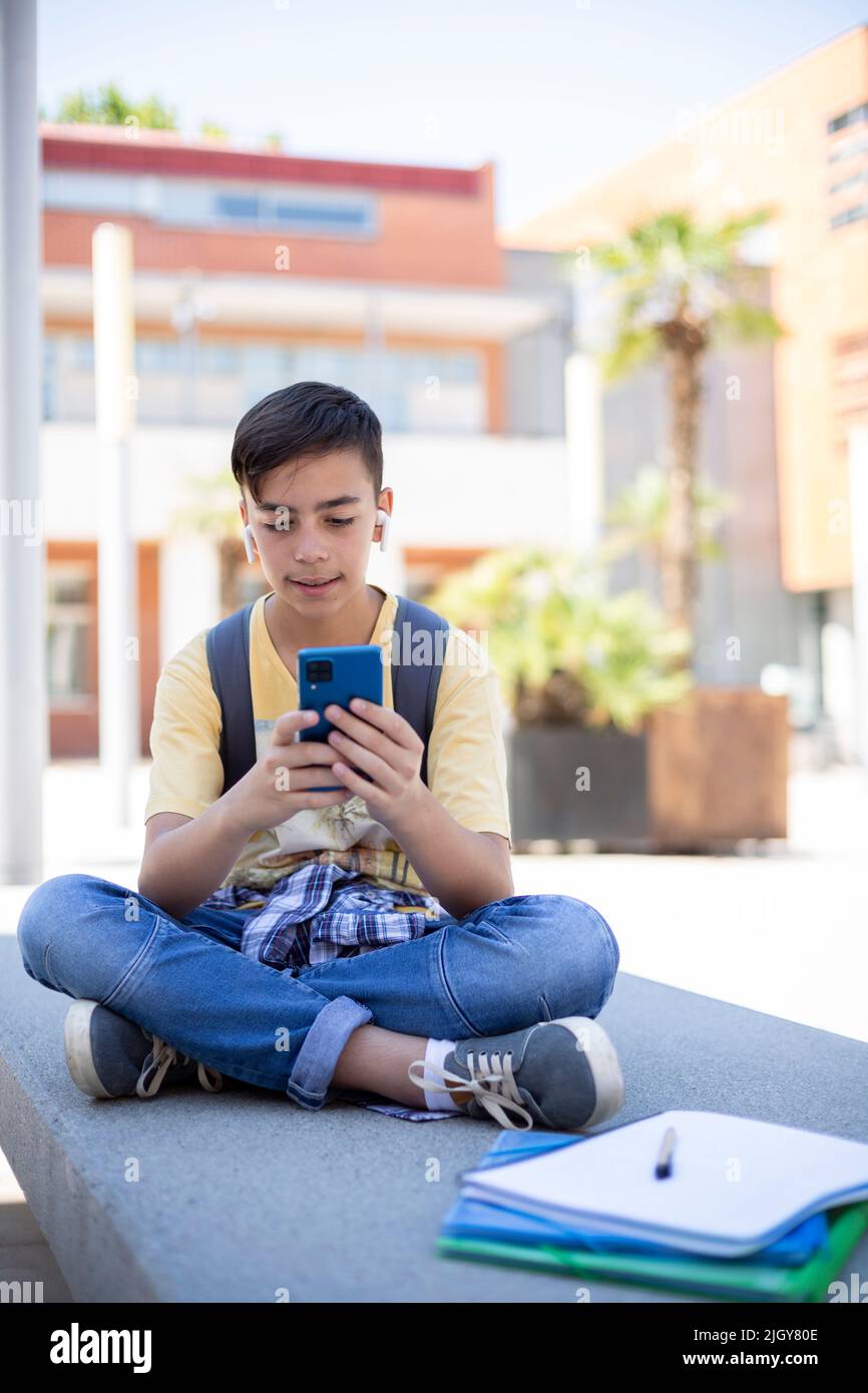 Un garçon d'un élève du secondaire utilisant un smartphone à l'extérieur de l'école. Espace pour le texte. Banque D'Images