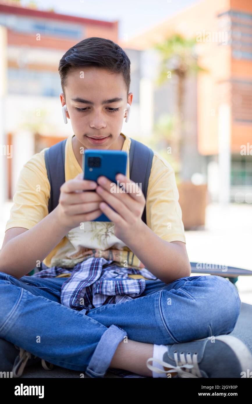 Portrait d'un adolescent de race blanche en utilisant un téléphone portable à l'extérieur de l'école secondaire. Banque D'Images