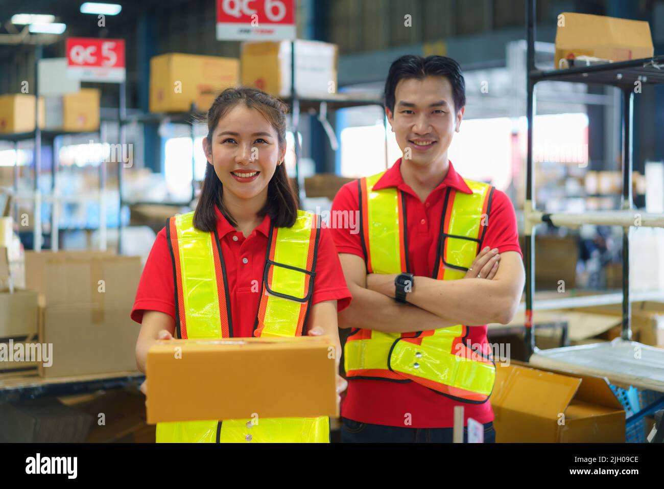 Une jeune femme et un jeune homme tenant un emballage en carton travaillant dans un entrepôt entre des rayonnages et des étagères se préparent pour le service qui déplace les commandes de marchandises. Banque D'Images