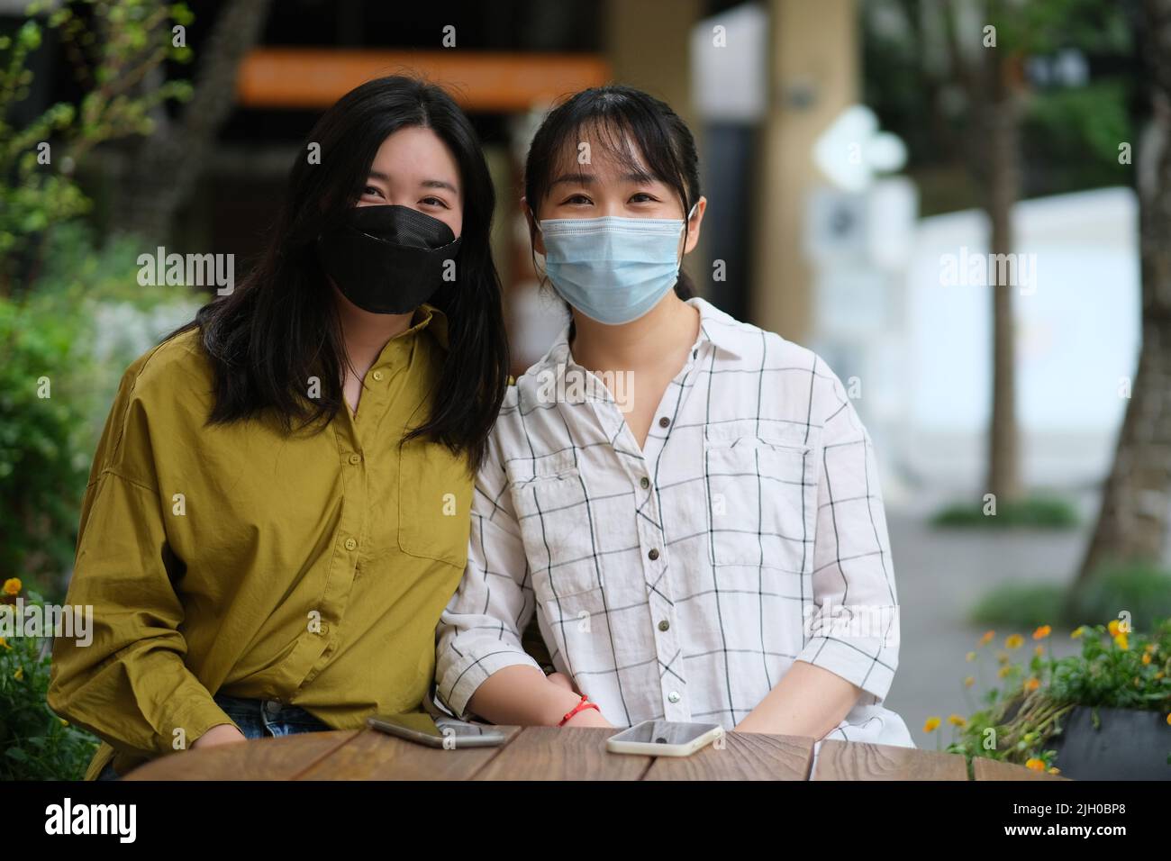 Deux jeunes femmes asiatiques dans un masque facial assis au café-terrasse, regardant la caméra Banque D'Images
