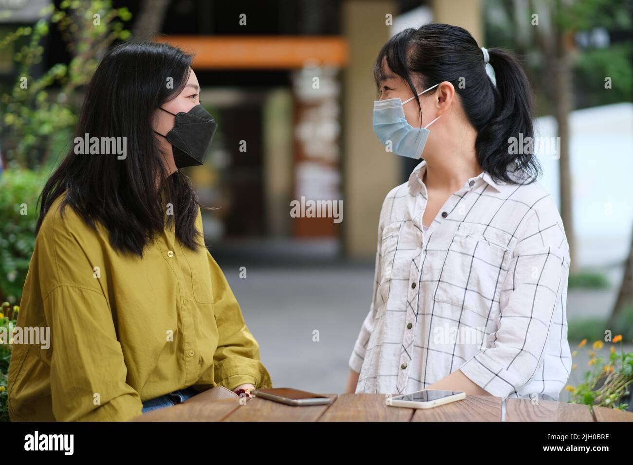 Deux jeunes femmes asiatiques en masque facial, parlent l'une à l'autre au café-terrasse Banque D'Images