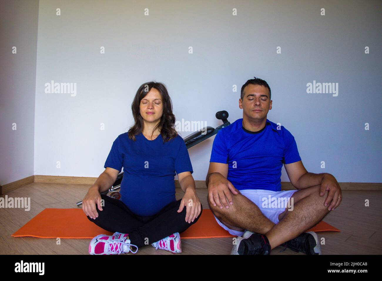 Image d'une jeune femme enceinte avec son mari dans la salle de gym à la maison tout en faisant la méditation et le yoga. Préparation physique et mentale pour l'accouchement Banque D'Images
