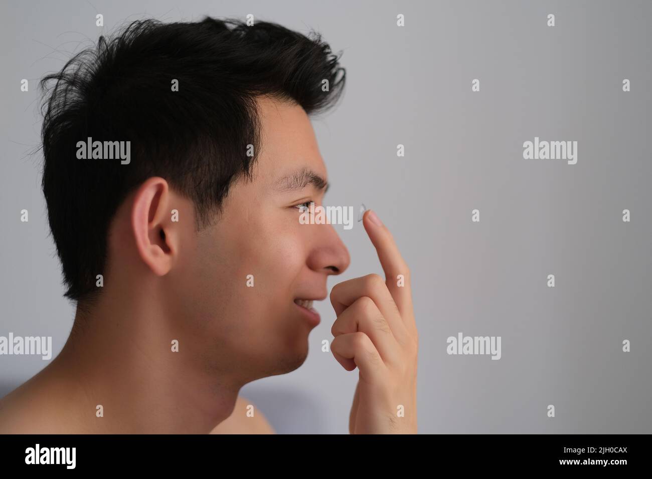 Profil visage de beau jeune homme asiatique appliquant des lentilles de contact Banque D'Images