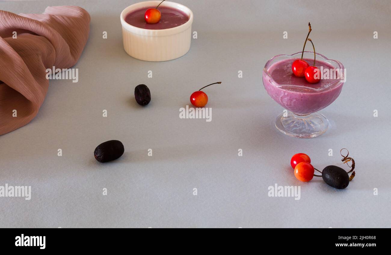 Vue de devant des bols à soupe Jamun, dessert traditionnel français d'été avec fruits Jamun et garnitures de cerise sur fond bleu clair. Banque D'Images