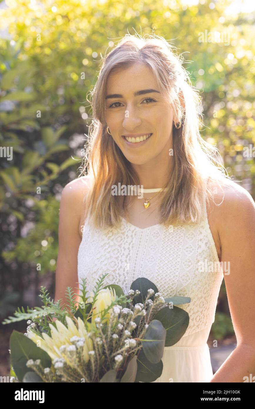 Image verticale de la bonne femme caucasienne en robe de mariage tenant des fleurs Banque D'Images