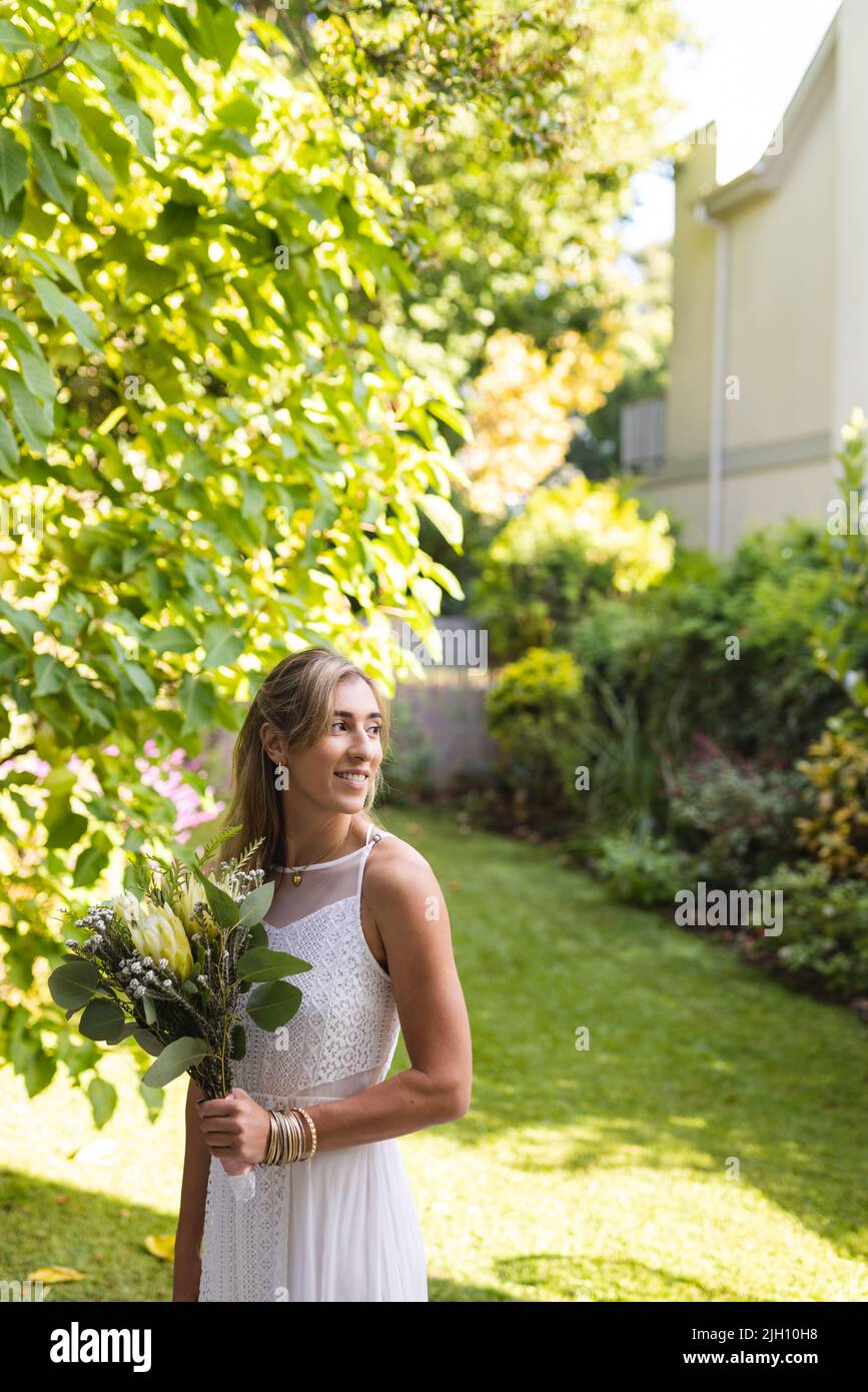 Image verticale de la bonne femme caucasienne en robe de mariage tenant des fleurs Banque D'Images