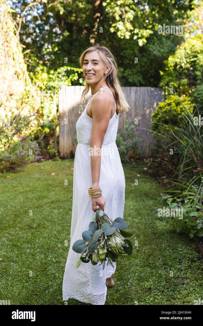 Image verticale de la bonne femme caucasienne en robe de mariage tenant des fleurs Banque D'Images