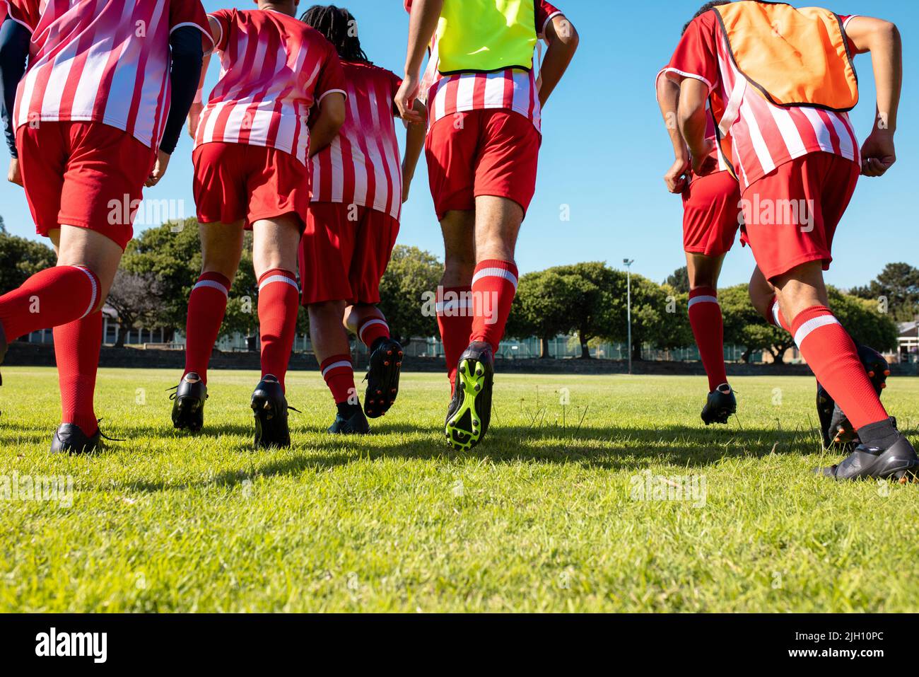 Vue en contre-plongée des athlètes masculins multiraciaux en uniforme rouge et chaussures de football sur terre herbeuse Banque D'Images